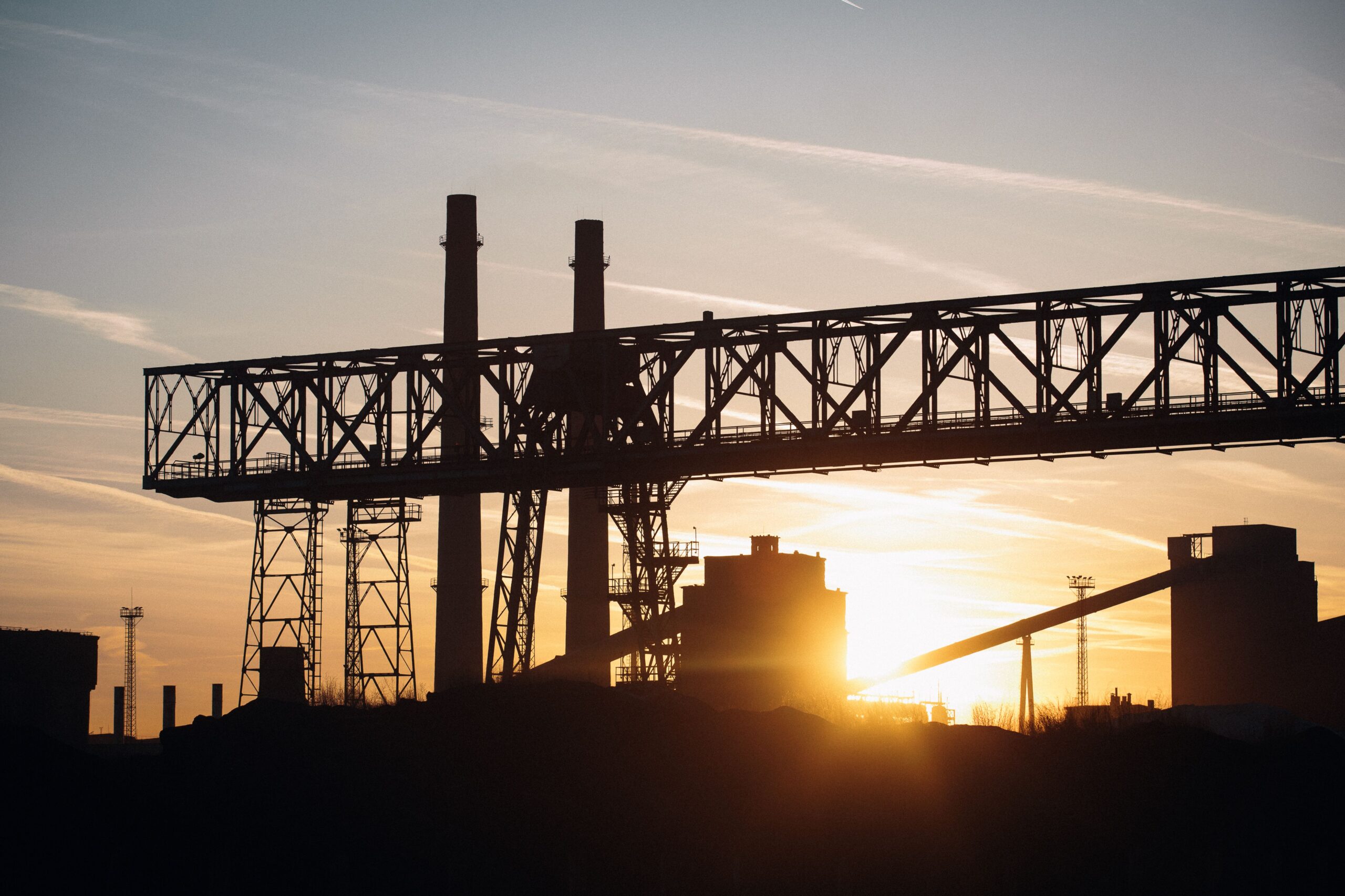 Silhouette of an industrial structure against a sunset sky, symbolizing industry and energy.